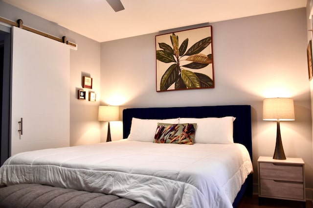 bedroom with a barn door, ceiling fan, and wood-type flooring