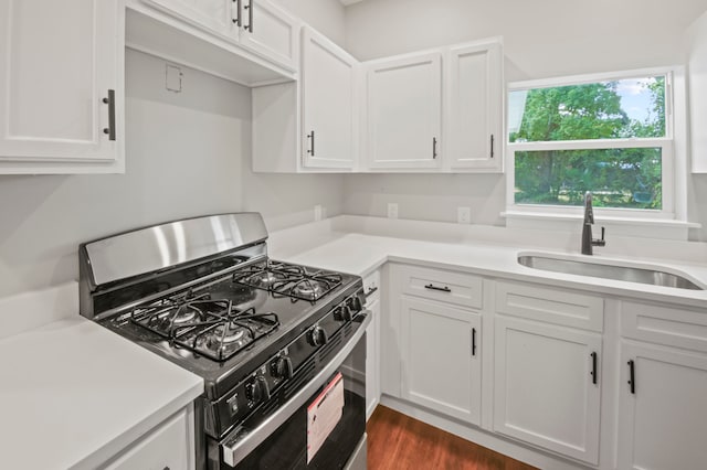 kitchen with dark wood-type flooring, stainless steel range with gas cooktop, sink, and white cabinets