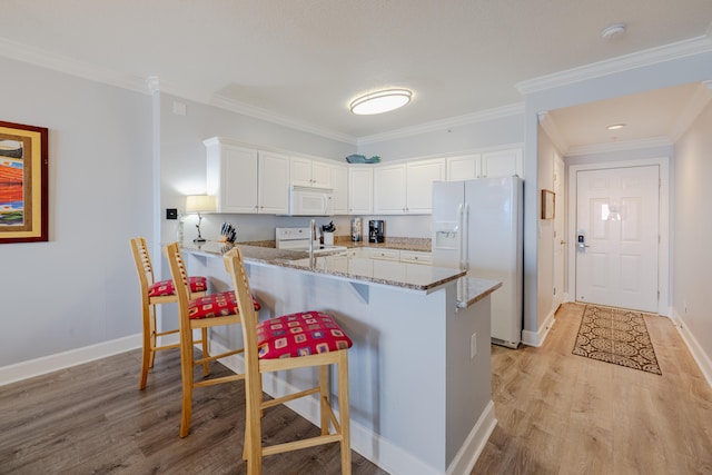 kitchen with kitchen peninsula, a kitchen breakfast bar, white cabinetry, light stone counters, and white appliances