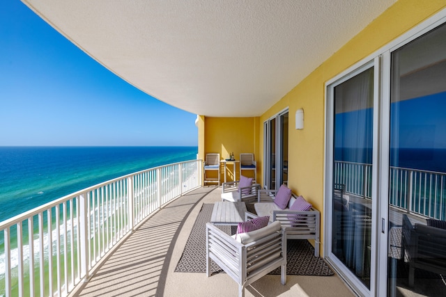 balcony with an outdoor living space, a water view, and a beach view