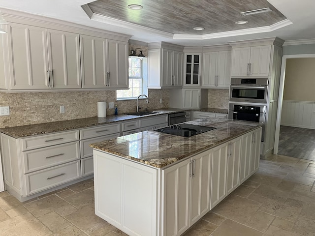 kitchen featuring stone tile floors, a tray ceiling, a sink, and a center island