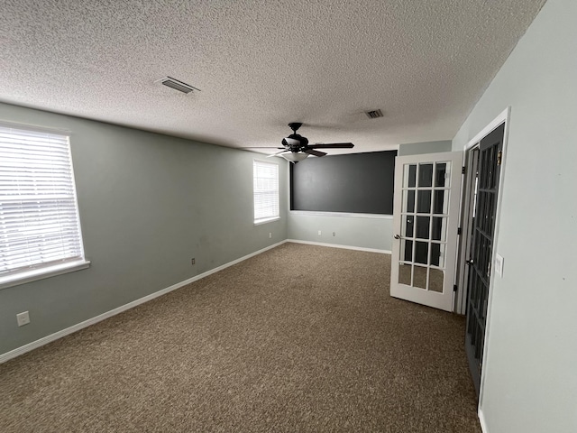 unfurnished room with ceiling fan, dark colored carpet, visible vents, and baseboards