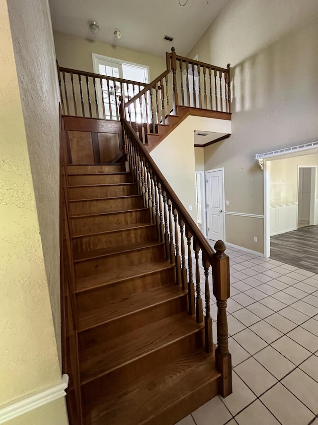 stairs featuring visible vents, a textured wall, a towering ceiling, baseboards, and tile patterned floors