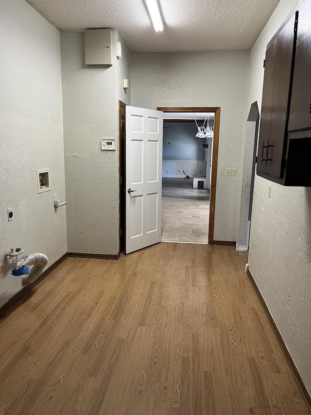 hallway featuring light wood-style floors, a textured wall, a textured ceiling, and baseboards