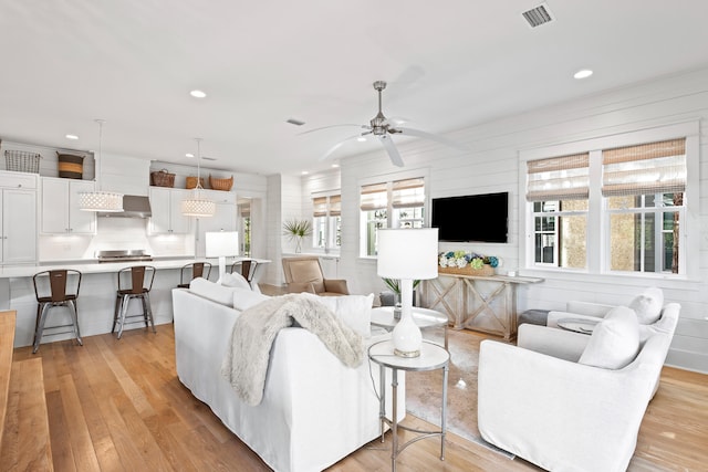 living room with wood walls, ceiling fan, and light hardwood / wood-style flooring