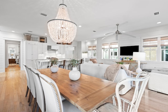 dining area with light wood-type flooring, wooden walls, and ceiling fan with notable chandelier