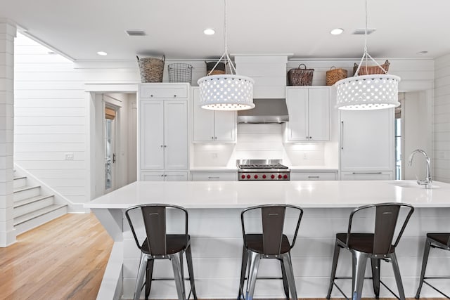 kitchen featuring sink, a breakfast bar, light hardwood / wood-style flooring, white cabinets, and stainless steel range