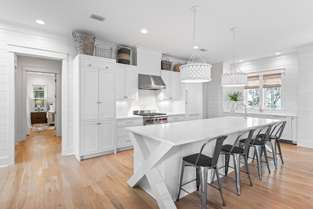 kitchen with white cabinetry, wall chimney range hood, light wood-type flooring, stainless steel range, and a breakfast bar area