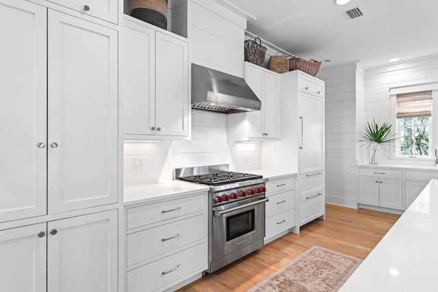 kitchen featuring white cabinetry, wall chimney range hood, premium range, and light wood-type flooring