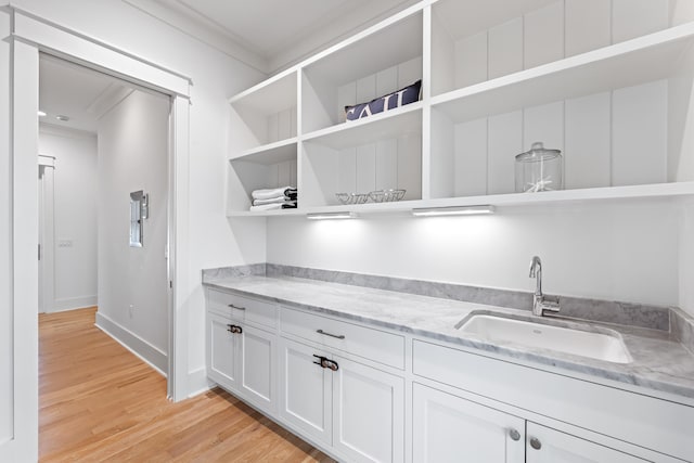 kitchen with light hardwood / wood-style floors, white cabinets, sink, crown molding, and light stone countertops