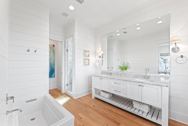 bathroom with ornamental molding, wood-type flooring, vanity, a bath, and wooden walls