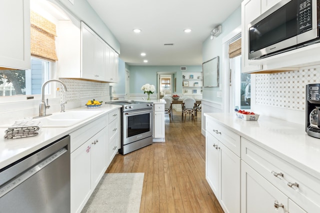 kitchen featuring tasteful backsplash, appliances with stainless steel finishes, sink, light wood-type flooring, and white cabinets