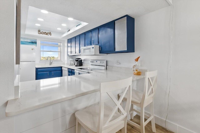 kitchen featuring white appliances, sink, a kitchen bar, a tray ceiling, and blue cabinets