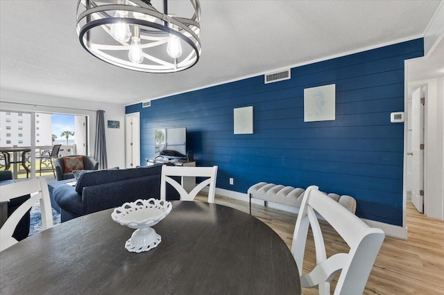 dining area featuring wooden walls, a notable chandelier, a textured ceiling, and light wood-type flooring