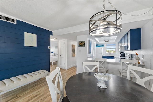 dining room with light hardwood / wood-style floors, a notable chandelier, a textured ceiling, and wood walls