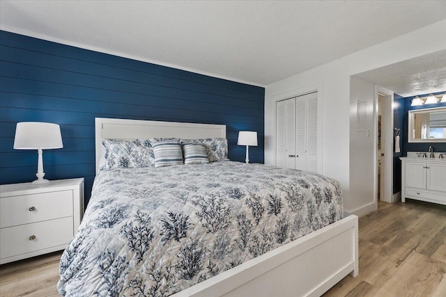 bedroom featuring a textured ceiling, light wood-type flooring, wooden walls, a closet, and sink