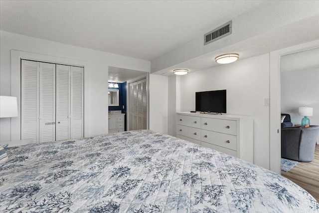 bedroom with light hardwood / wood-style floors, a textured ceiling, and multiple closets