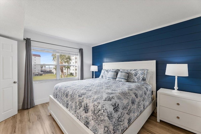 bedroom featuring a textured ceiling, light wood-type flooring, and wood walls