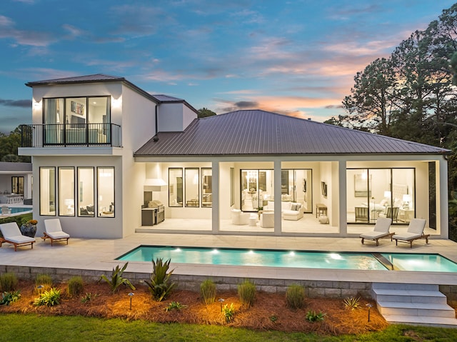 back house at dusk featuring outdoor lounge area, a balcony, and a patio