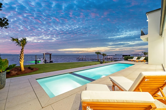 pool at dusk with an in ground hot tub, a yard, a water view, and a patio area