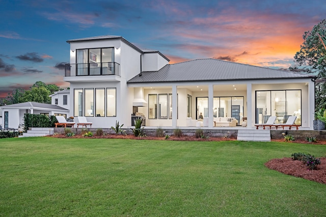 back house at dusk featuring a balcony and a lawn