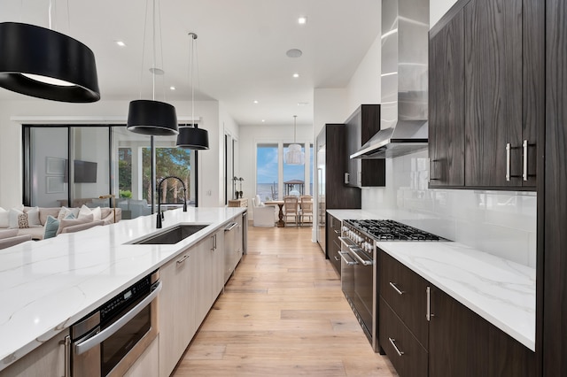 kitchen with sink, light hardwood / wood-style flooring, wall chimney exhaust hood, appliances with stainless steel finishes, and decorative light fixtures