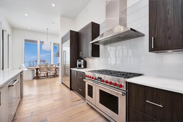 kitchen featuring tasteful backsplash, hanging light fixtures, high end appliances, exhaust hood, and light wood-type flooring