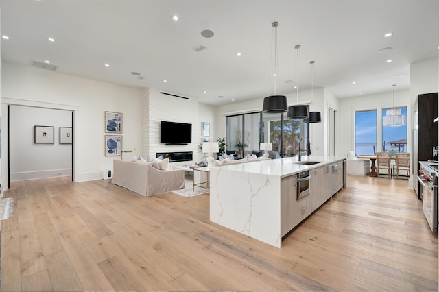 kitchen with a large island with sink, sink, light hardwood / wood-style flooring, and decorative light fixtures