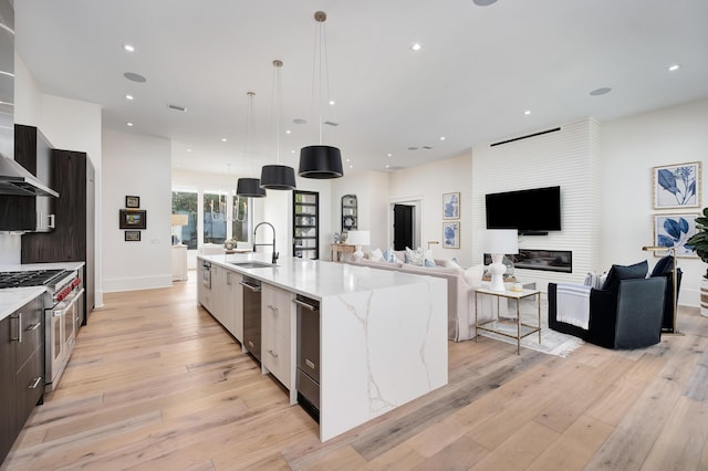 kitchen with sink, high end range, hanging light fixtures, light stone countertops, and a large island with sink