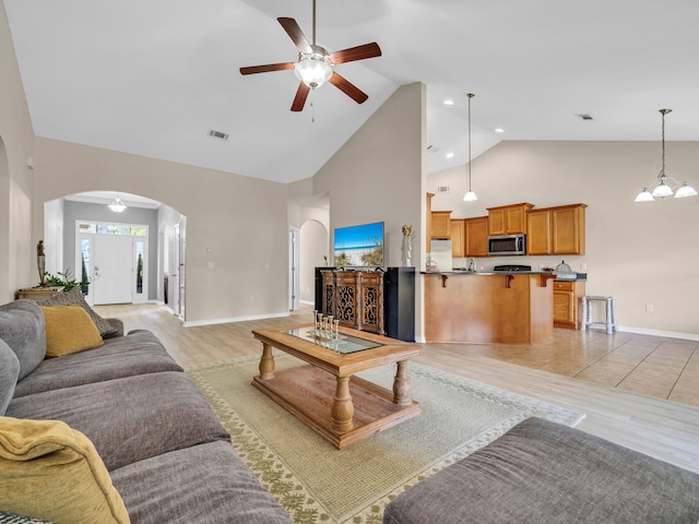 living room with high vaulted ceiling, light hardwood / wood-style floors, and ceiling fan with notable chandelier