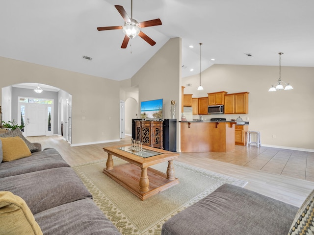 living room with ceiling fan with notable chandelier, light wood-type flooring, and high vaulted ceiling