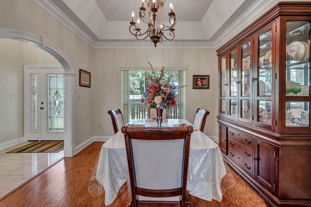 dining area with an inviting chandelier, ornamental molding, a tray ceiling, and light wood-type flooring