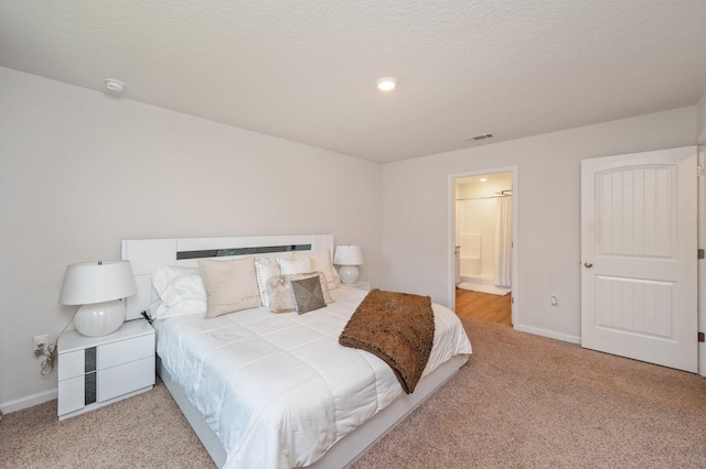 bedroom featuring a textured ceiling, light colored carpet, and ensuite bath