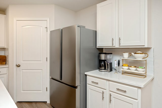 kitchen with stainless steel refrigerator, white cabinetry, light wood-type flooring, and decorative backsplash