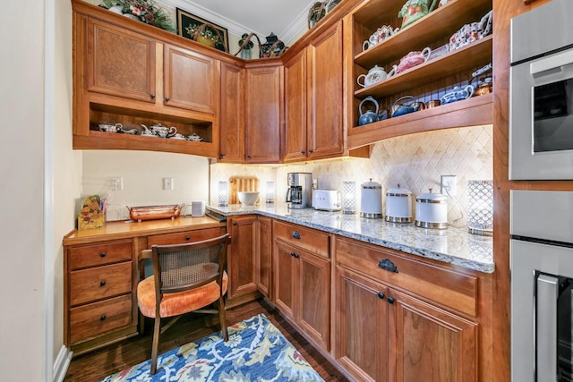 kitchen with decorative backsplash, built in desk, wall oven, light stone counters, and dark hardwood / wood-style flooring