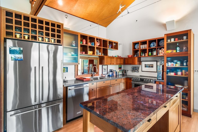 kitchen featuring a kitchen island, light hardwood / wood-style flooring, stainless steel appliances, dark stone countertops, and sink