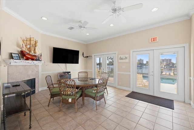 dining space with french doors, a tile fireplace, ceiling fan, crown molding, and light tile patterned floors