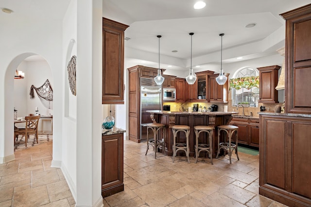 kitchen featuring a kitchen bar, a center island, hanging light fixtures, built in appliances, and dark stone countertops