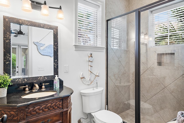 bathroom with vanity, a shower with shower door, toilet, and ceiling fan