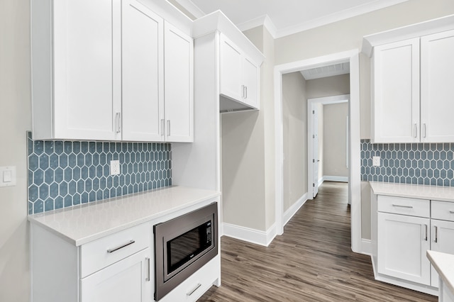 kitchen with backsplash, stainless steel microwave, ornamental molding, and white cabinets