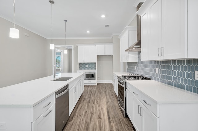 kitchen with stainless steel appliances, hanging light fixtures, sink, white cabinetry, and wall chimney range hood