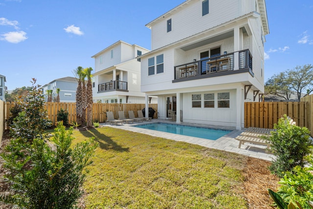 back of house featuring a balcony, a patio area, a fenced in pool, and a lawn