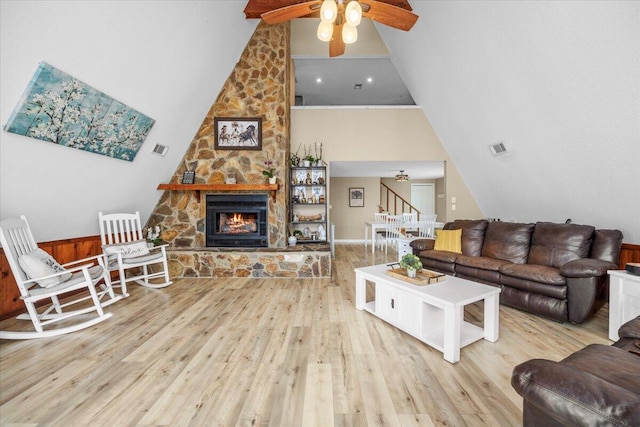 living room featuring a stone fireplace, light wood-type flooring, ceiling fan, and high vaulted ceiling