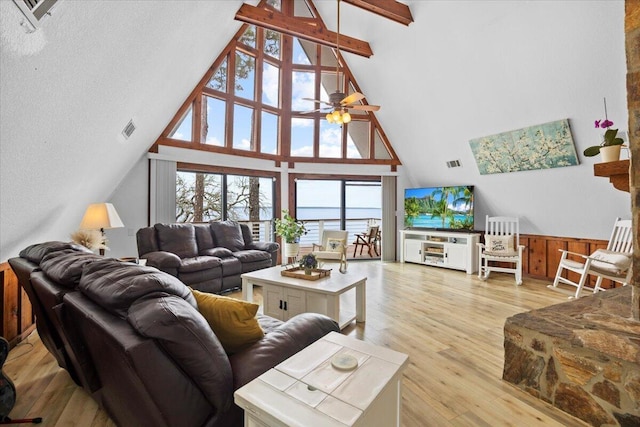 living room featuring light wood-type flooring, high vaulted ceiling, wooden walls, beamed ceiling, and ceiling fan