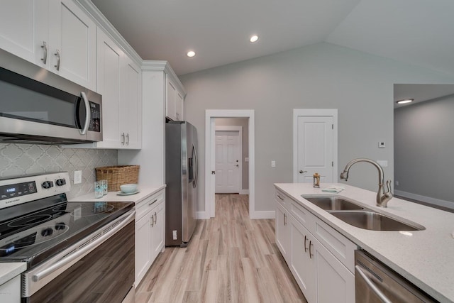 kitchen with appliances with stainless steel finishes, backsplash, vaulted ceiling, sink, and white cabinets