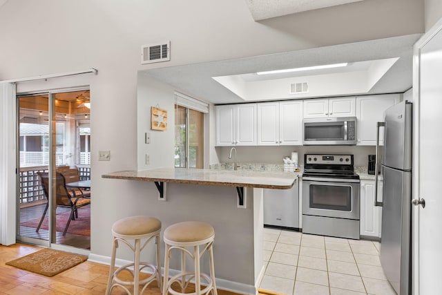 kitchen with a kitchen bar, kitchen peninsula, stainless steel appliances, and white cabinets