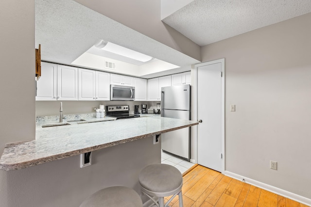 kitchen with kitchen peninsula, appliances with stainless steel finishes, a kitchen bar, white cabinets, and light wood-type flooring