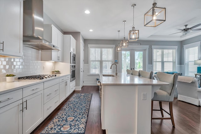 kitchen with white cabinetry, a center island with sink, a kitchen breakfast bar, stainless steel appliances, and wall chimney range hood