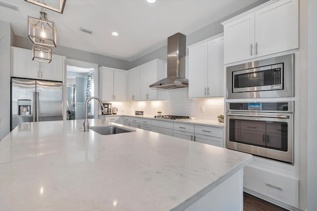 kitchen featuring sink, appliances with stainless steel finishes, white cabinetry, hanging light fixtures, and wall chimney exhaust hood