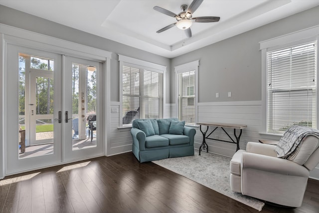 living room with a tray ceiling, dark wood-type flooring, and ceiling fan